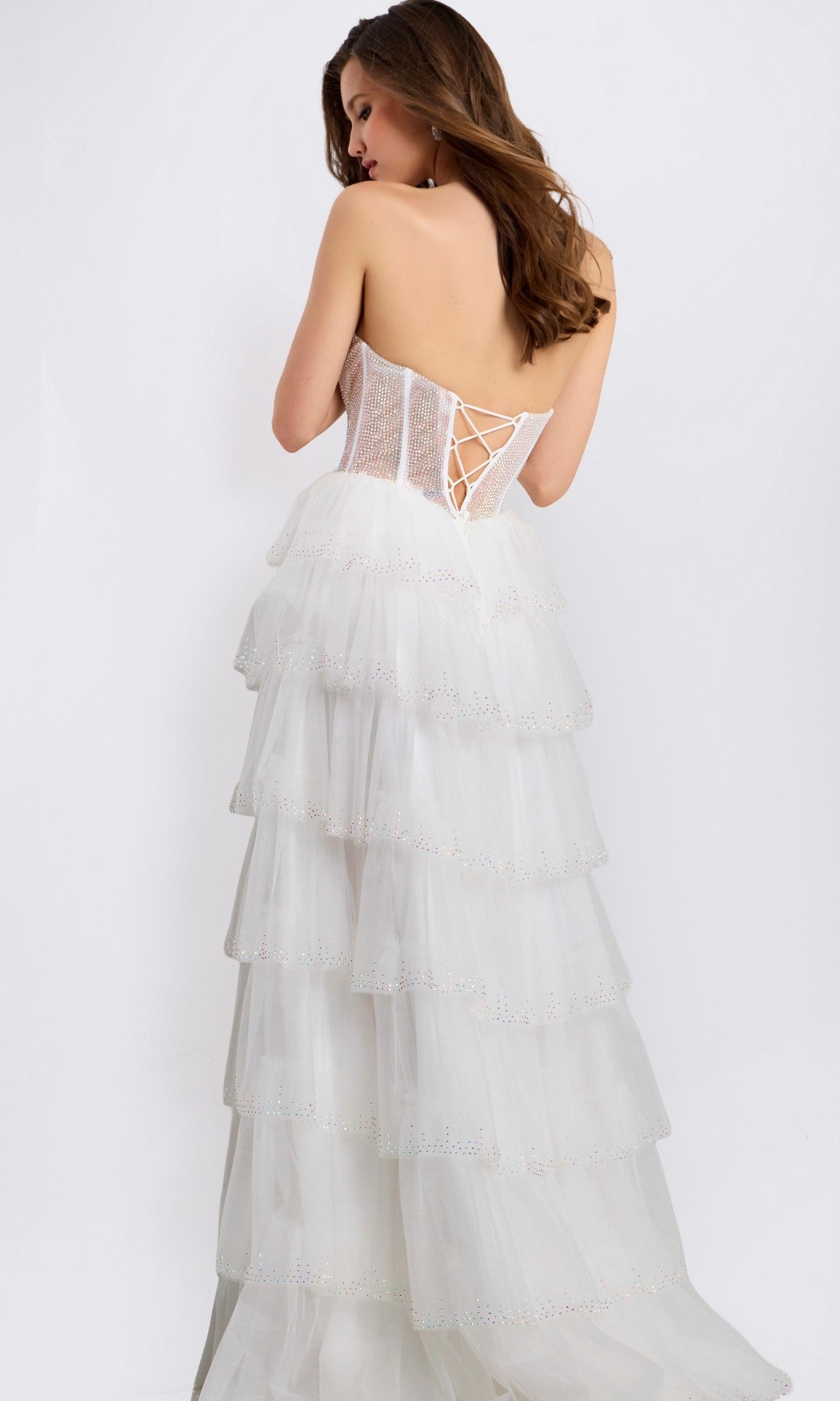 A woman models the Jovani 47290 long prom dress, featuring a strapless white tiered gown with a corset-style bodice and lace-up back, posing with her back to the camera against a plain white background.
